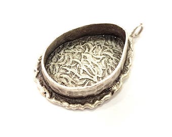 May include: Silver pendant with a decorative, ornate design on the back. The pendant is oval shaped and has a loop for attaching a chain.
