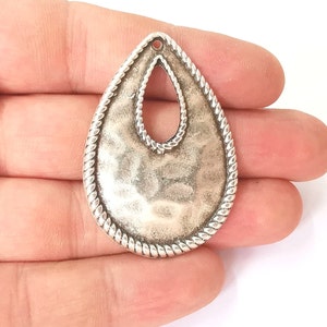 Peut inclure: Pendentif en argent en forme de larme avec une surface texturée et une bordure en forme de corde. Le pendentif a un grand trou au centre.