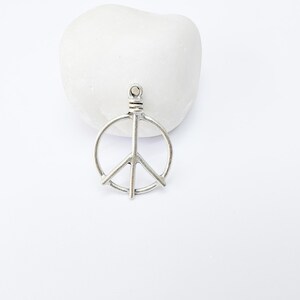 May include: Silver peace sign charm pendant. The charm is a simple, open circle design with a peace sign inside.