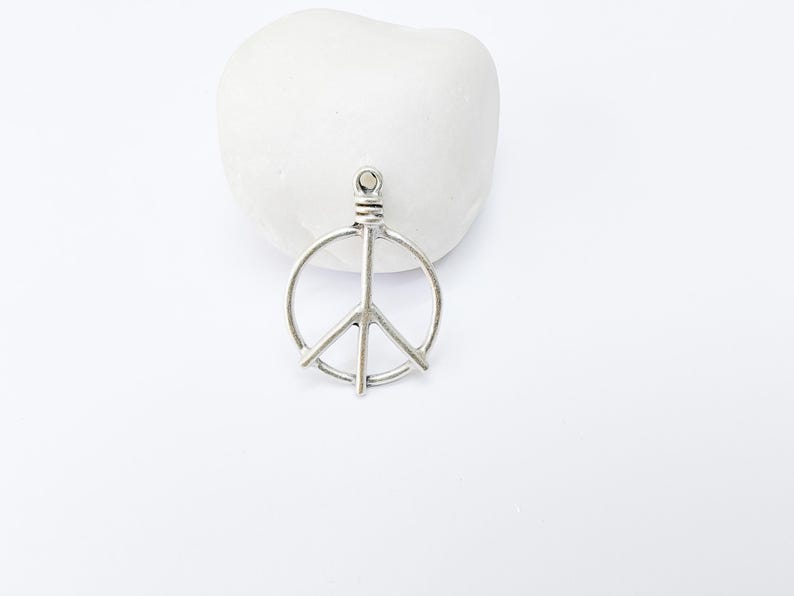May include: Silver peace sign charm pendant. The charm is a simple, open circle design with a peace sign inside.