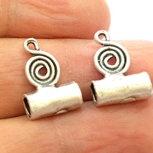 May include: Two silver-toned metal end caps for jewelry making. Each cap features a decorative spiral design and a cylindrical barrel.