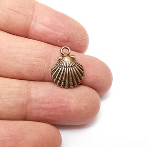 Op de afbeelding: Een koperkleurige schelpbedel met een gedetailleerd ontwerp. De bedel heeft een lus aan de bovenkant om aan sieraden of andere knutselwerken te bevestigen.