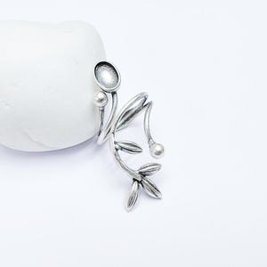May include: Silver ring with a twisted branch design and leaves. The ring has a round, open space on the top.