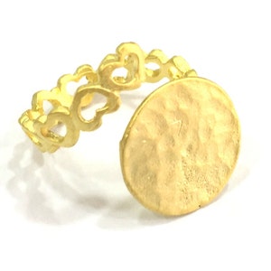 May include: Gold ring with a heart-shaped band and a round, hammered disc. The disc is slightly oval-shaped and has a textured surface.