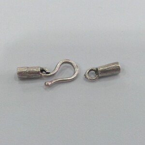 May include: Silver-toned metal clasp with a hook and a barrel-shaped end piece. The clasp is designed for jewelry making.