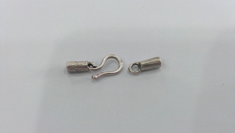 May include: Silver-toned metal clasp with a hook and a barrel-shaped end piece. The clasp is designed for jewelry making.