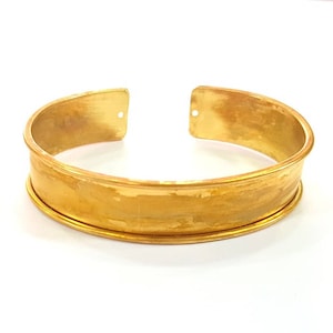 May include: A gold-toned metal bangle bracelet with a hammered finish. The bracelet has a wide band and a slightly rounded shape.
