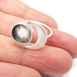 Puede incluir: Un anillo de plata con un diseño de media luna y un engaste redondo. El engaste está lleno de un material blanco y brillante.