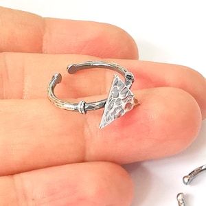 Könnte beinhalten: Ein silberner Ring mit einem strukturierten Dreiecksdesign. Der Ring ist offen und verstellbar.