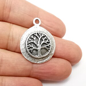 May include: Silver charm with a tree of life design. The charm is round and has a textured surface.