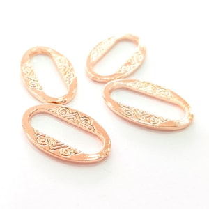 May include: Four rose gold oval-shaped metal rings with a decorative pattern. The rings are designed to be used as connectors for jewelry making.