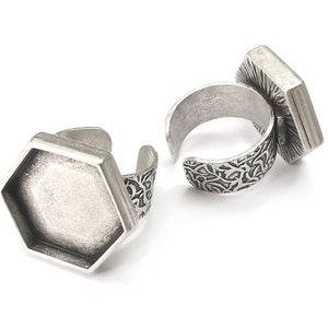 May include: Two silver-toned adjustable rings. One ring features a hexagonal bezel, the other a rectangular bezel. Both rings have an open design and decorative etched bands. The rings are displayed on a white background.