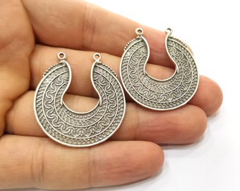 Puede incluir: Dos abalorios de pendientes de metal plateado con un diseño circular intrincado y ornamentado. Los abalorios tienen un bucle en la parte superior para sujetarlos a los pendientes.