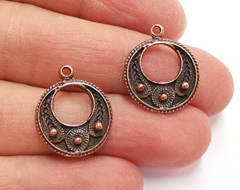May include: Two copper-colored metal earring blanks with a circular design. The blanks have a decorative pattern around the edge and three raised circles in the center.