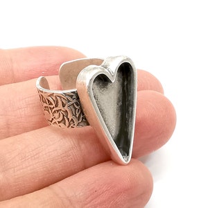 May include: Silver ring with a heart-shaped bezel. The ring band is decorated with a floral pattern.