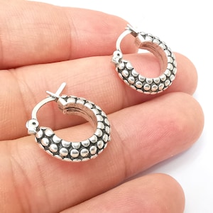 May include: A pair of silver hoop earrings with a textured, beaded design.