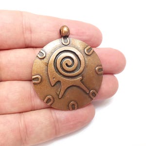 May include: A copper-toned pendant with a circular design featuring a stylized spiral and a horseshoe pattern around the edge.