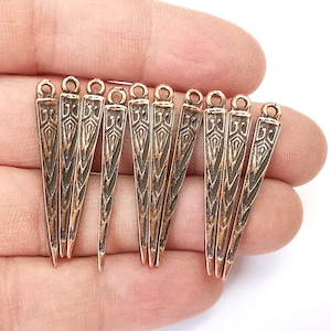 Puede incluir: Diez abalorios de metal de color cobre en forma de punta afilada con intrincados diseños geométricos. Los abalorios tienen un bucle en la parte superior para sujetarlos a joyas u otras manualidades.