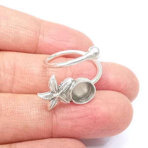May include: Silver ring featuring a starfish design and a round bezel setting. The ring is adjustable and can be worn on any finger.
