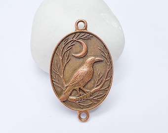 Op de afbeelding: Koperkleurige ovale hanger met een gedetailleerd ontwerp van een raaf op een tak, met een halve maan op de achtergrond. De hanger heeft lussen om aan een ketting of andere sieradenonderdelen te bevestigen.