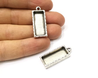 May include: Two silver-toned rectangular pendant trays with a textured border. The trays have a loop at the top for attaching to a chain or cord.