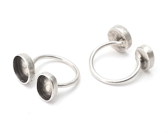 May include: Two silver rings with round, open-backed settings. The rings are designed to hold small cabochons or other decorative elements.