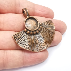 May include: A copper-toned pendant with a fan-shaped design and a round, open-backed bezel. The pendant has a textured surface and a loop at the top for attaching a chain.
