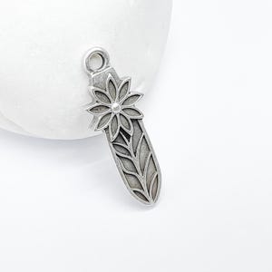 Op de afbeelding: Zilveren bedel met een bloem- en bladontwerp. De bedel is ovaalvormig en heeft een lus aan de bovenkant om aan een armband of ketting te bevestigen.