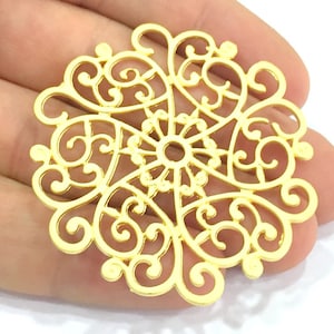 Op de afbeelding: Gouden filigraan metalen bedel met een cirkelvormig ontwerp. De bedel heeft een delicaat, ingewikkeld patroon van spiralen en lussen.