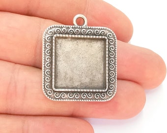 May include: Silver-toned square pendant with a decorative border and a blank square space in the center. The pendant has a loop at the top for attaching a chain.