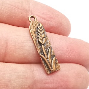 May include: A copper-colored charm with a detailed wheat stalk design. The charm has a textured surface and a loop at the top for attaching to a necklace or bracelet.