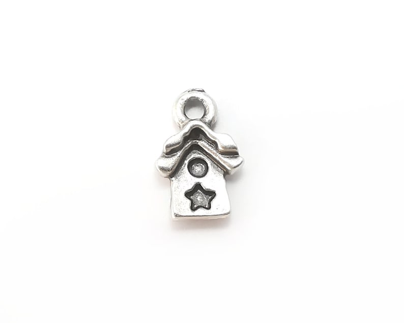 May include: Silver charm in the shape of a birdhouse with a star on the front.