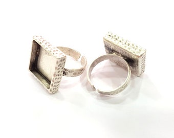 May include: Close-up of two silver-toned adjustable rings with rectangular settings. The settings have a textured, hammered appearance. The rings are on a white background, showcasing the jewelry's design and craftsmanship.