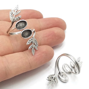May include: Two silver rings with a leaf design and two round open spaces for stones. The rings are on a hand.
