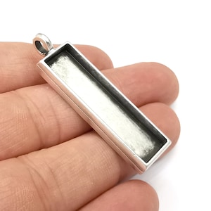 May include: Silver pendant with a rectangular bezel for resin or other materials. The pendant has a loop at the top for attaching a chain.