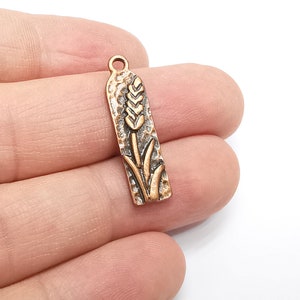 May include: A copper-toned metal charm with a wheat stalk design. The charm has a textured surface and a loop at the top for attaching to a necklace or bracelet.