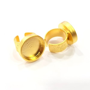 Op de afbeelding: Twee ringvormige bases van goudkleur voor het maken van sieraden. Elke basis heeft een ronde, platte bovenkant met een gladde, glanzende afwerking.