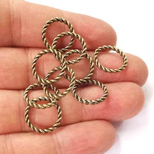 Peut inclure: Un groupe de huit anneaux de saut en métal doré avec un design de corde torsadée. Les anneaux sont disposés en pile sur une main.