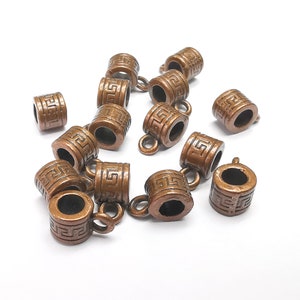 Op de afbeelding: Een groep van 12 antieke koperkleurige metalen eindkappen met een decoratief Grieks sleutelpatroon. Elke eindkap heeft een kleine lus om aan een koord of ketting te bevestigen.