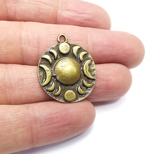 May include: A bronze pendant featuring a sun and moon design. The sun is in the centre of the pendant and is surrounded by a circle of crescent moons.