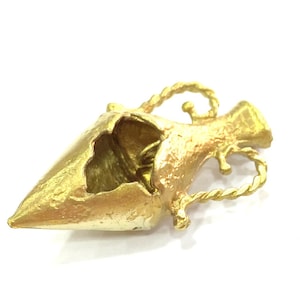 Peut inclure: Un pendentif en métal doré en forme de vase avec un motif de corde torsadée. Le vase a un trou sur le côté et il manque une partie du haut.