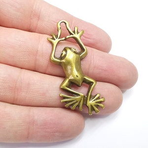 May include: A gold-toned metal frog charm with a loop for hanging. The frog is in a jumping pose with its legs outstretched.
