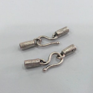 May include: Two silver metal hook and loop clasps for jewelry making. Each clasp has a textured barrel and a hook.