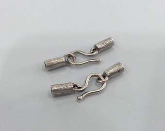 May include: Two silver metal hook and loop clasps for jewelry making. Each clasp has a textured barrel and a hook.