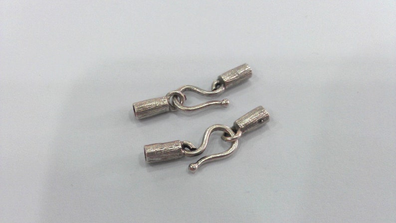 May include: Two silver metal hook and loop clasps for jewelry making. Each clasp has a textured barrel and a hook.