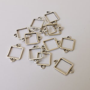 May include: A collection of silver-coloured square connector charms with small loops on each side. The charms have a slightly distressed finish, and are scattered across a light grey surface. These charms are ideal for jewellery making and crafting.