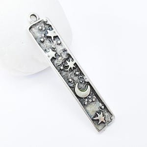 May include: Silver charm with a crescent moon and stars design. The charm is rectangular and has a textured surface.