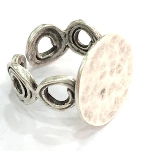 May include: Silver ring with a round, textured, silver-toned metal base. The ring has a decorative, openwork design with multiple loops.