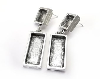 May include: A pair of silver earrings with a rectangular design. The earrings have a small square at the top and a larger rectangle hanging below. The earrings are made of metal and have a textured finish.