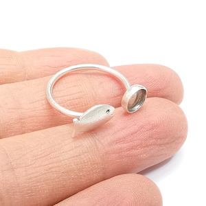 May include: Silver ring with a fish design and a round bezel setting. The ring is open on one side and the fish is attached to the ring.